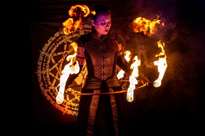 Artiste de feu exécutant un numéro avec des flammes, fond sombre et symboles occultes.