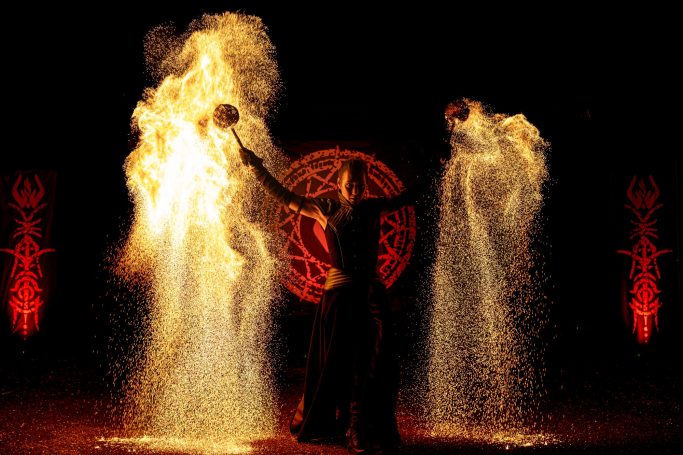 Performeur de feu dans une ambiance sombre avec des motifs rouges en arrière-plan.
