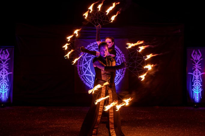 Artiste de feu en performance, maniant des éventails de feu sous des lumières colorées.