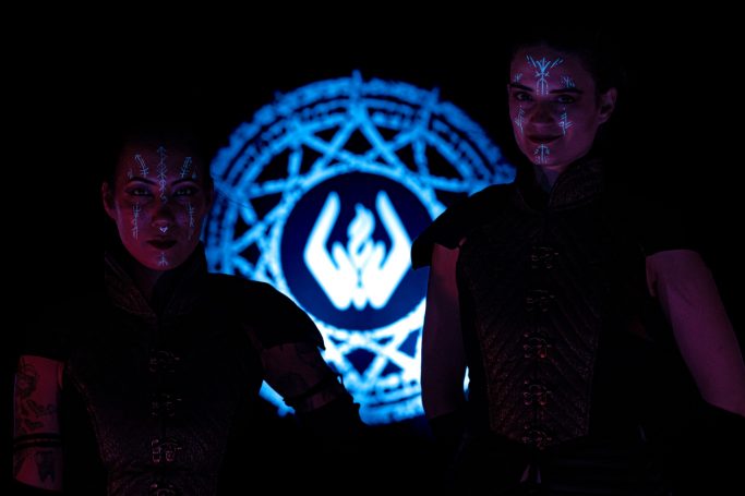 Deux personnages mystérieux, éclairés par une lumière bleue avec un symbole derrière eux.